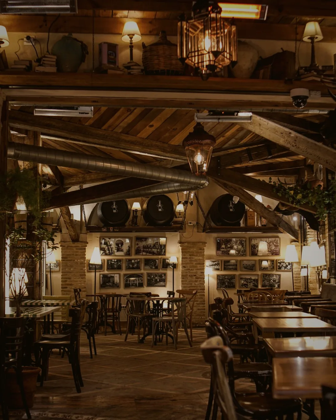 A warmly lit dining room with exposed timber beams, lamplight and long wooden tables.